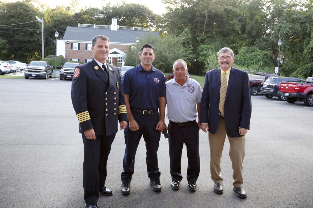 Four men pose for a photo outside of the fire department headquarters.